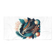 A white beach towel featuring a central graphic print of a sea turtle surrounded by tropical leaves, coral, and seashells in teal, orange, and dark gray.