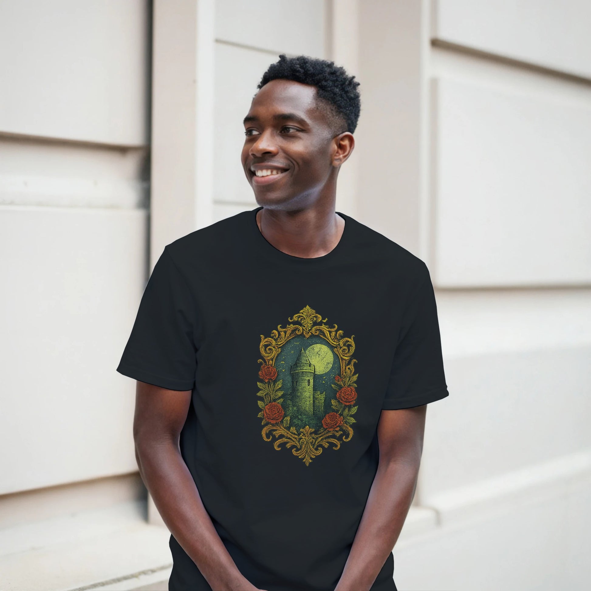 Man wearing a black t-shirt with a decorative design of a castle and roses, standing against a light-colored wall.
