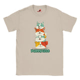 A flat lay sand T-shirt featuring a colorful graphic of four stacked cartoon puppies in teal, orange, cream, and yellow shades with the words “Puppy Love” in playful green text below

