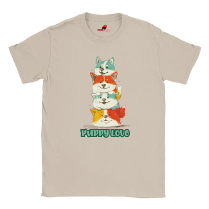 A flat lay sand T-shirt featuring a colorful graphic of four stacked cartoon puppies in teal, orange, cream, and yellow shades with the words “Puppy Love” in playful green text below

