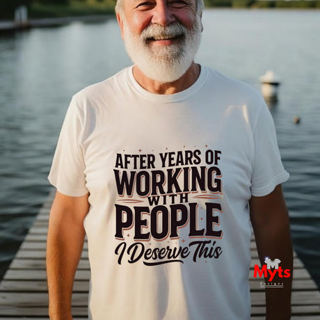 An older man with a white beard stands on a wooden dock by the water wearing a white graphic t-shirt with the text 'AFTER YEARS OF WORKING WITH PEOPLE I DESERVE THIS' in black and brown lettering. A red 'Myts' brand logo is visible in the bottom right corner.