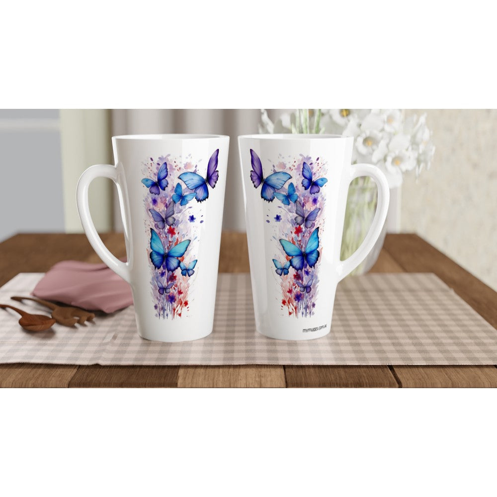 Two tall white ceramic mugs with butterfly and floral watercolor designs in blue, purple, and pink, displayed on a checkered placemat on a wooden table.