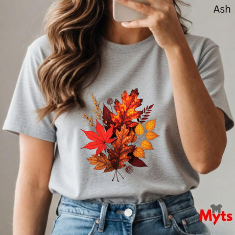 Person wearing a gray t-shirt with autumn leaf design, holding a phone.