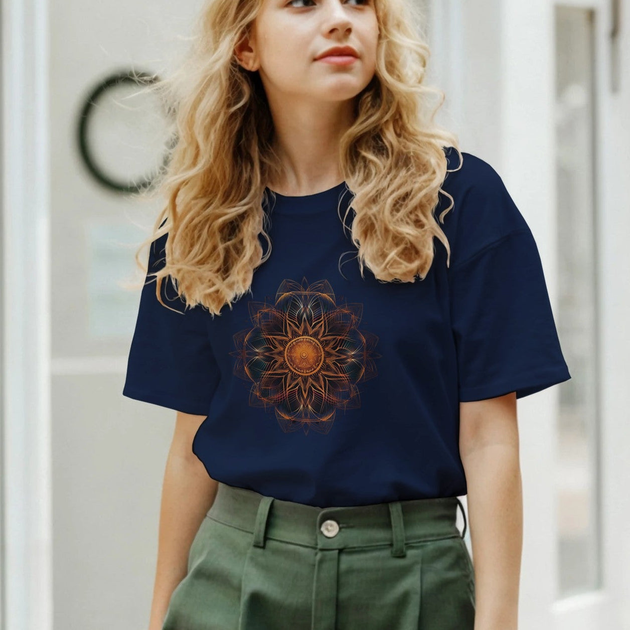 A woman wearing a navy blue t-shirt with a mandala design and green pants outdoors.