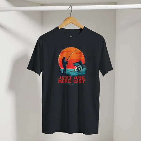 Black t-shirt with a fishing graphic and 'Just One More Cast' text on a hanger against a white wall.