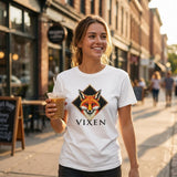 Woman wearing a white t-shirt with a fox graphic and 'VIXEN' text, holding a drink on a city street.