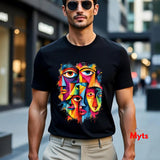 A man wearing a black short-sleeve t-shirt with a colorful abstract face graphic on the front, paired with beige trousers and sunglasses, standing in an outdoor urban setting.