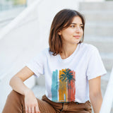 Woman wearing a white t-shirt with a colorful palm tree design, sitting on steps.