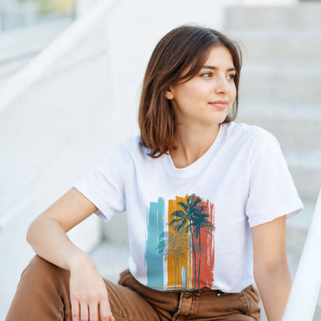 Woman wearing a white t-shirt with a colorful palm tree design, sitting on steps.
