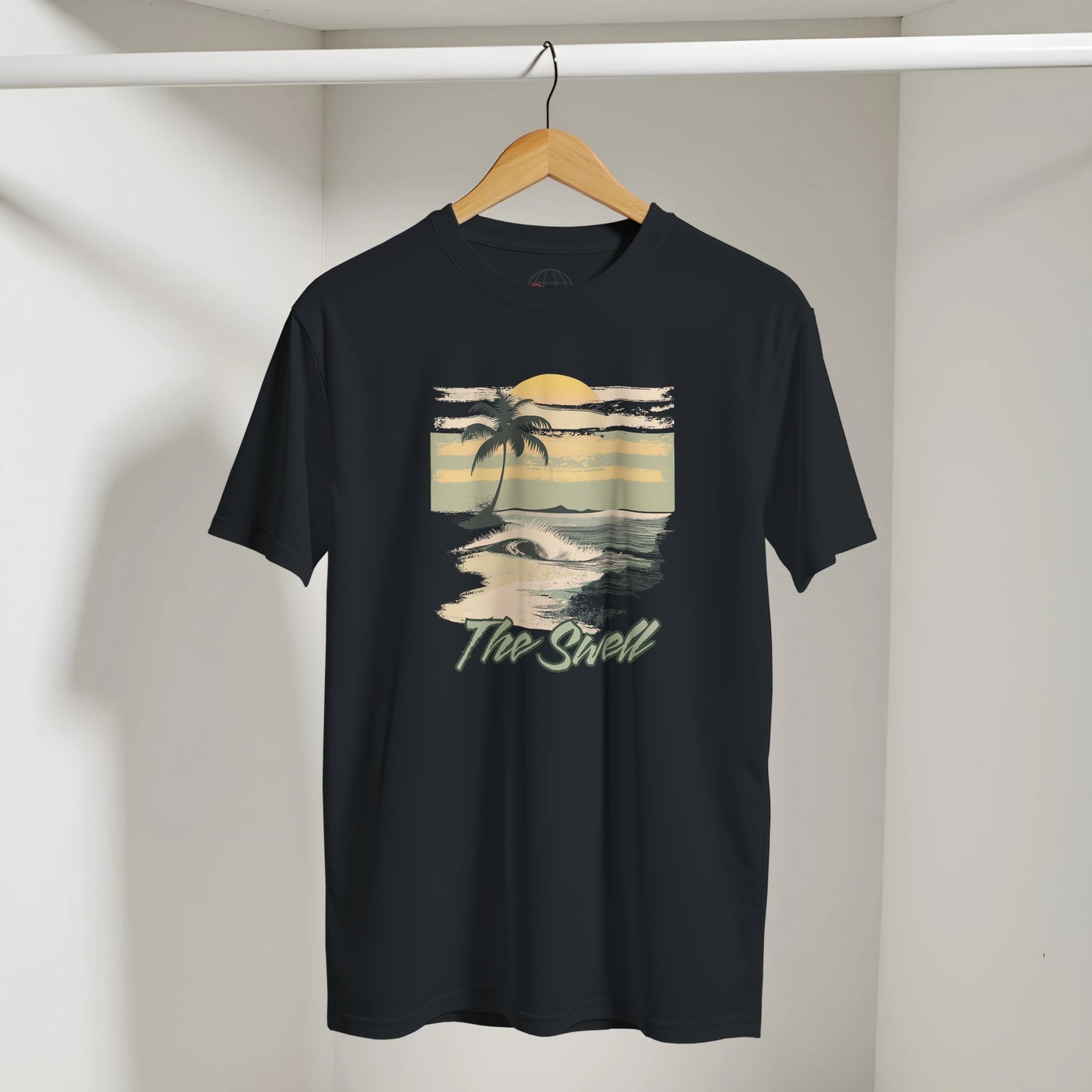 Black t-shirt with a beach graphic and 'The Shell' text on a hanger against a white wall.
