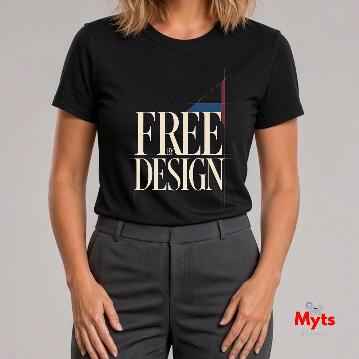 A woman wearing a black short-sleeve graphic T-shirt with the words 'FREE IN DESIGN' in large cream lettering and dark gray trousers, photographed against a light gray studio background. A small 'Myts' logo appears in the bottom right corner.