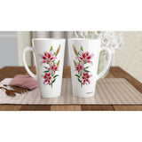 Two tall white ceramic mugs with pink and green lily floral prints, displayed side by side on a checkered placemat over a wooden table.
