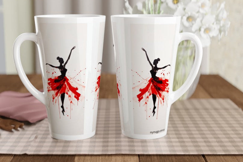 Two tall white ceramic mugs with black ballerina silhouettes and red paint-splatter tutus, displayed on a checkered placemat on a wooden table.