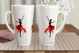 Two tall white ceramic mugs with black ballerina silhouettes and red paint-splatter tutus, displayed on a checkered placemat on a wooden table.