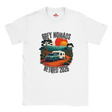 A white short-sleeve crewneck t-shirt featuring a retro-style graphic print of a grey pickup truck and a white camper van on an orange dirt road, with the text 'GREY NOMADS RETIRED 2026' and a sunset background.