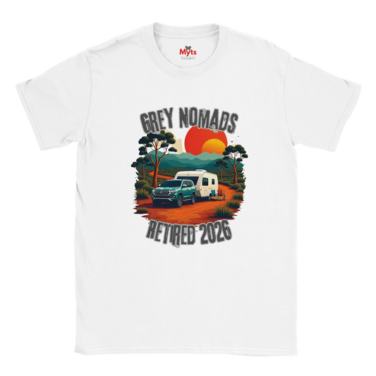 A white short-sleeve crewneck t-shirt featuring a retro-style graphic print of a grey pickup truck and a white camper van on an orange dirt road, with the text 'GREY NOMADS RETIRED 2026' and a sunset background.