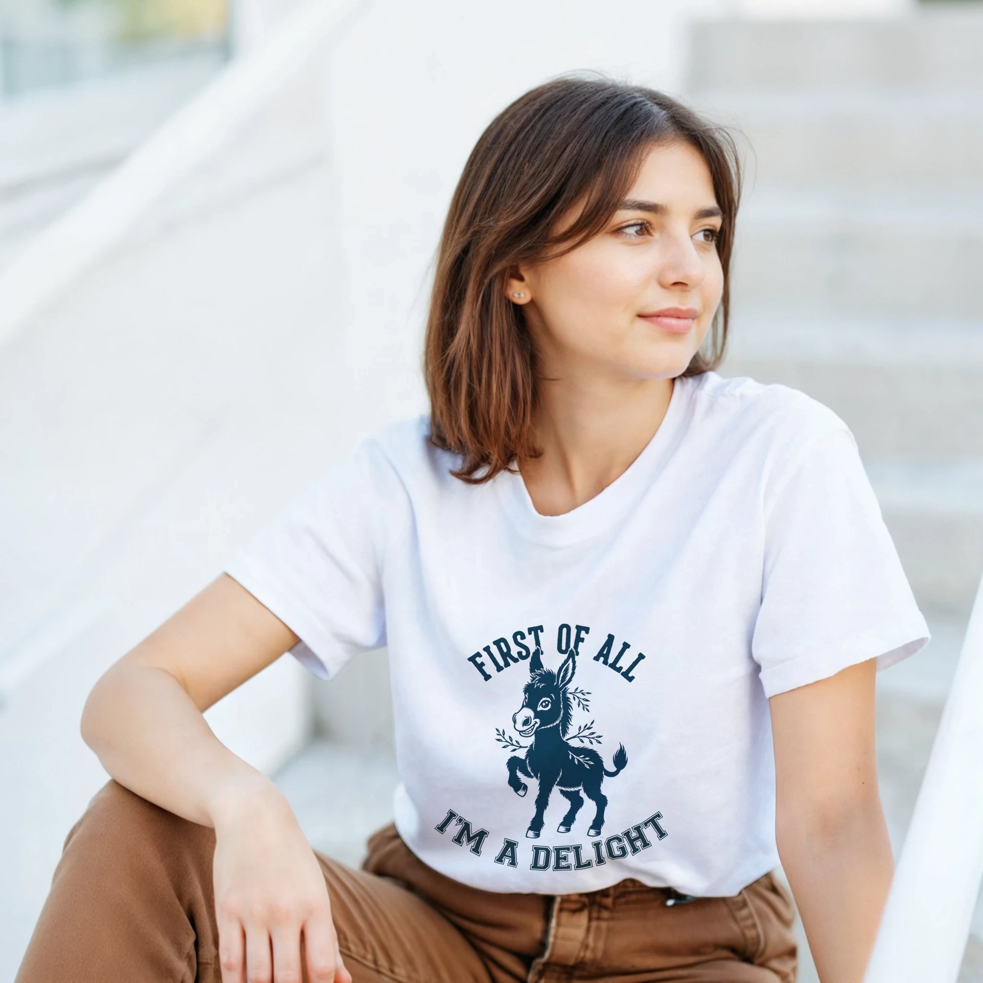 A woman wearing a white t-shirt with a 'Cute Donkey Design' design, sitting on the steps.