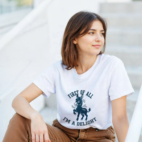 A woman wearing a white t-shirt with a 'Cute Donkey Design' design, sitting on the steps.
