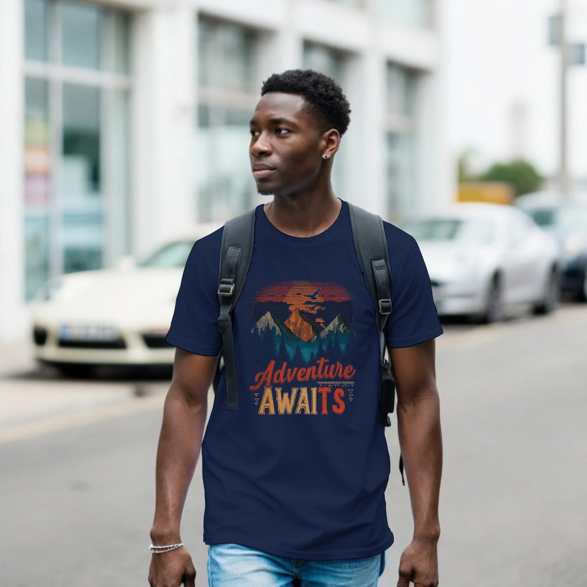 Man wearing a navy blue t-shirt with 'Adventure Awaits' graphic walking on a street.