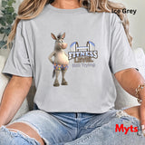 Woman seated in casual jeans wearing Ice Grey Fitness Level Still Trying humorous donkey graphic T-shirt.