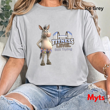 Woman seated in casual jeans wearing Ice Grey Fitness Level Still Trying humorous donkey graphic T-shirt.