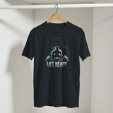 Black t-shirt with a graphic design of a person lifting weights and text 'Lift Heavy Become Unbreakable' on a hanger against a white wall.