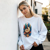 A woman wearing a white crewneck sweatshirt with a colorful seashell and starfish graphic, leaning against a white stucco wall outdoors.