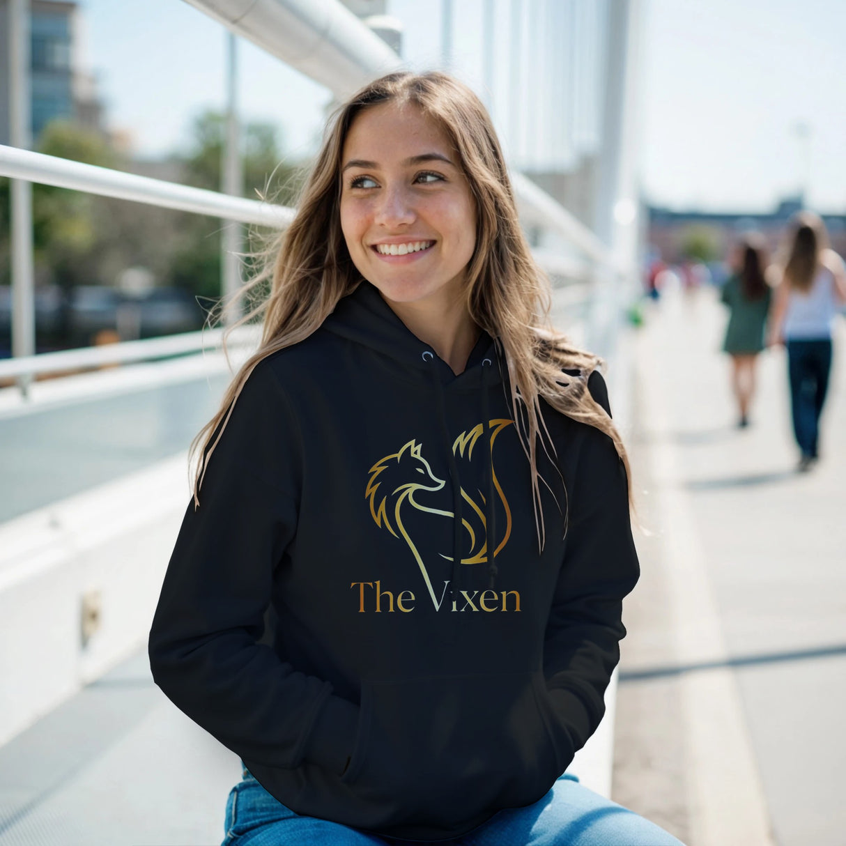 Woman wearing a black hoodie with a graphic design and text, sitting outdoors.
