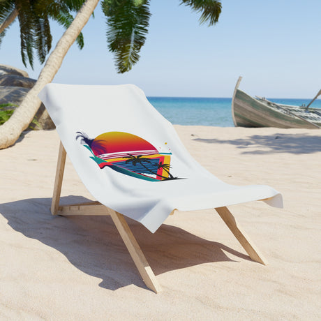 A white beach towel draped over a wooden lounge chair on a sandy tropical beach, featuring a colorful graphic of a sunset and palm trees.