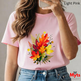 Person wearing a pink t-shirt with a colorful leaf design, holding a phone.