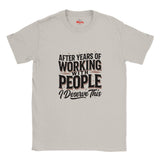 A light gray crewneck t-shirt with a humorous graphic printed on the front. The graphic reads 'AFTER YEARS OF WORKING WITH PEOPLE I DESERVE THIS' in black and dark brown lettering with thin red accent lines.