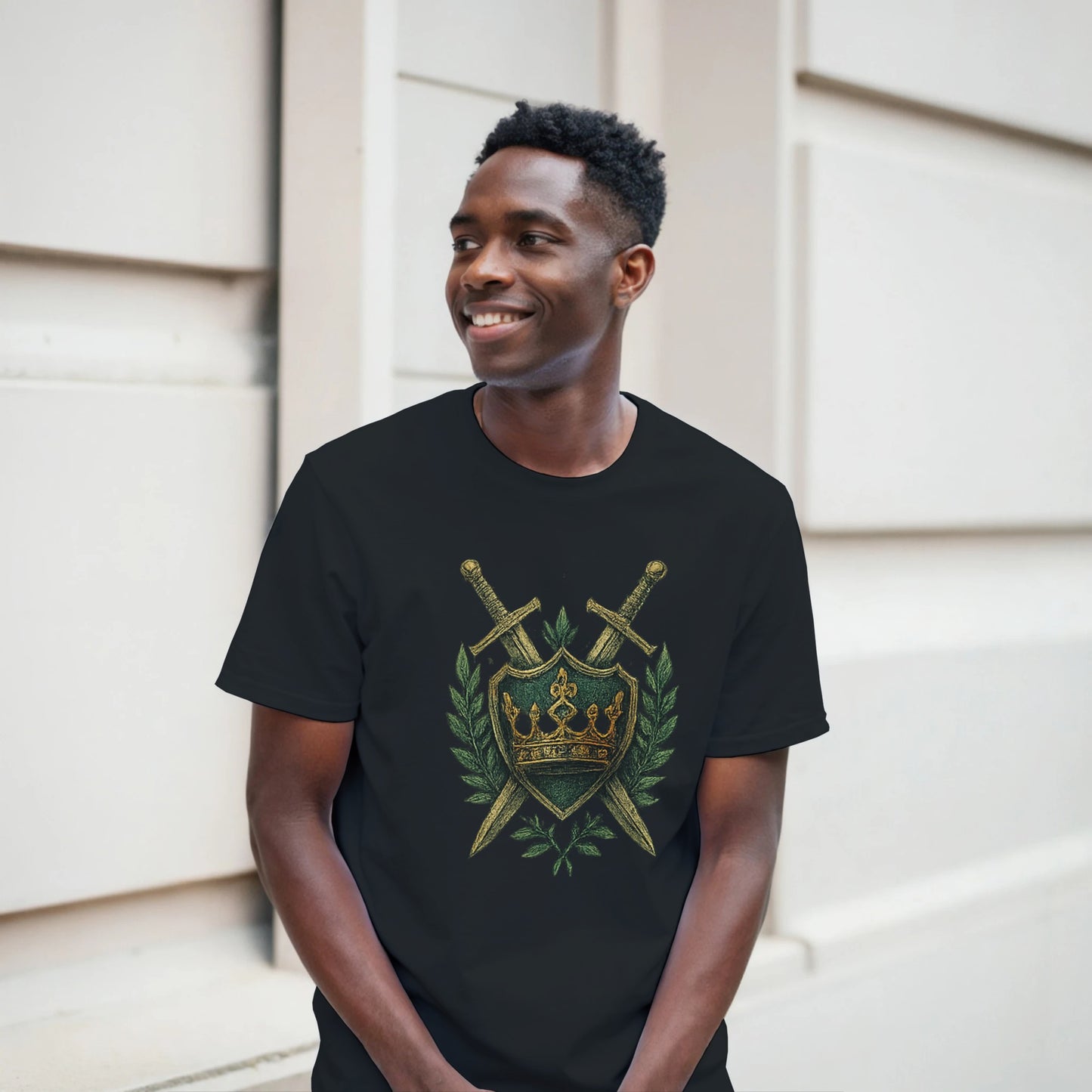 Man wearing a black t-shirt with a gold and green emblem design, standing against a light-colored wall.