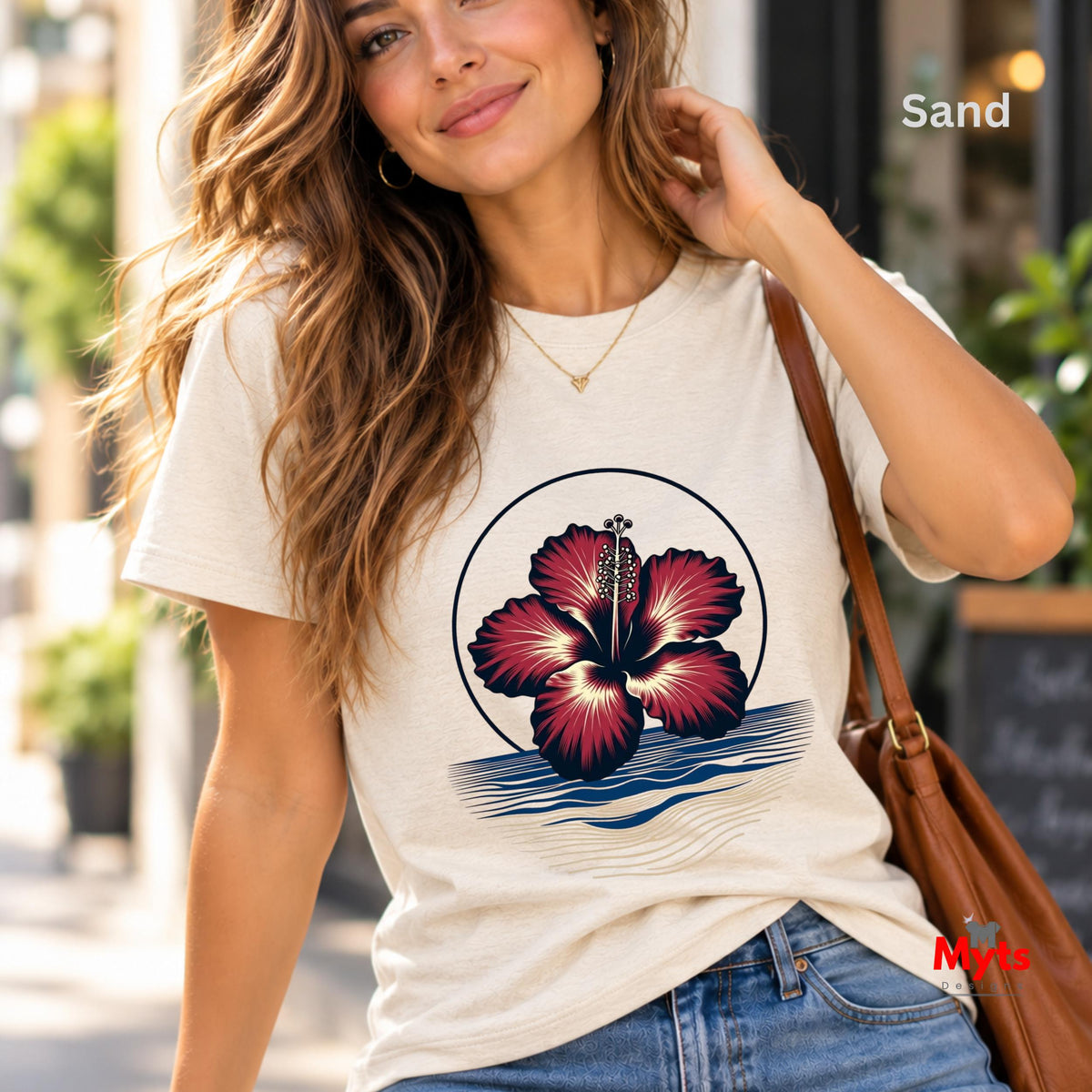 White tropical hibiscus flower graphic T-shirt featuring a vibrant red bloom, navy circular outline and stylised blue and sandy-gold ocean waves.