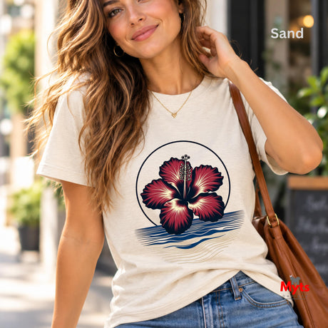 White tropical hibiscus flower graphic T-shirt featuring a vibrant red bloom, navy circular outline and stylised blue and sandy-gold ocean waves.
