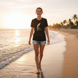 Woman walking on a beach at sunset wearing a black t-shirt with a logo.