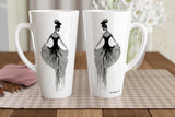 Two tall white ceramic mugs with black and gray watercolor-style illustrations of ballerinas, displayed on a checkered placemat on a wooden table.