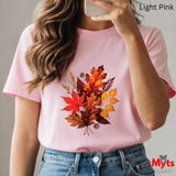 Person wearing a pink t-shirt with autumn leaf design, holding a phone.