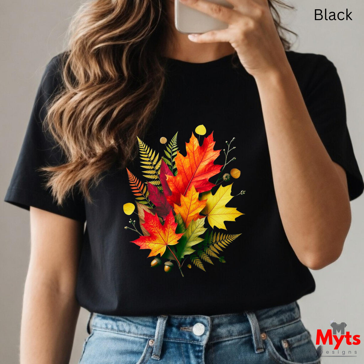 Person wearing a black t-shirt with colorful leaf design, holding a phone.