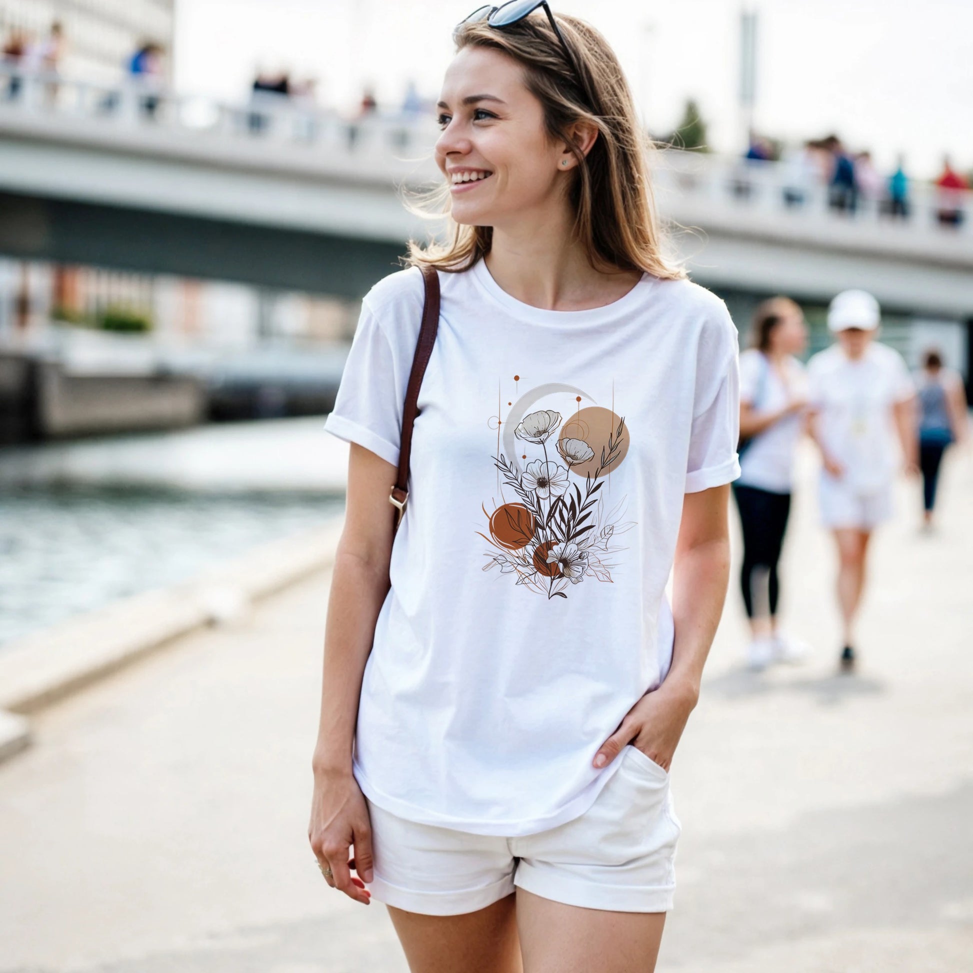 A woman wearing a white t-shirt with a graphic design, standing outdoors near a waterfront.