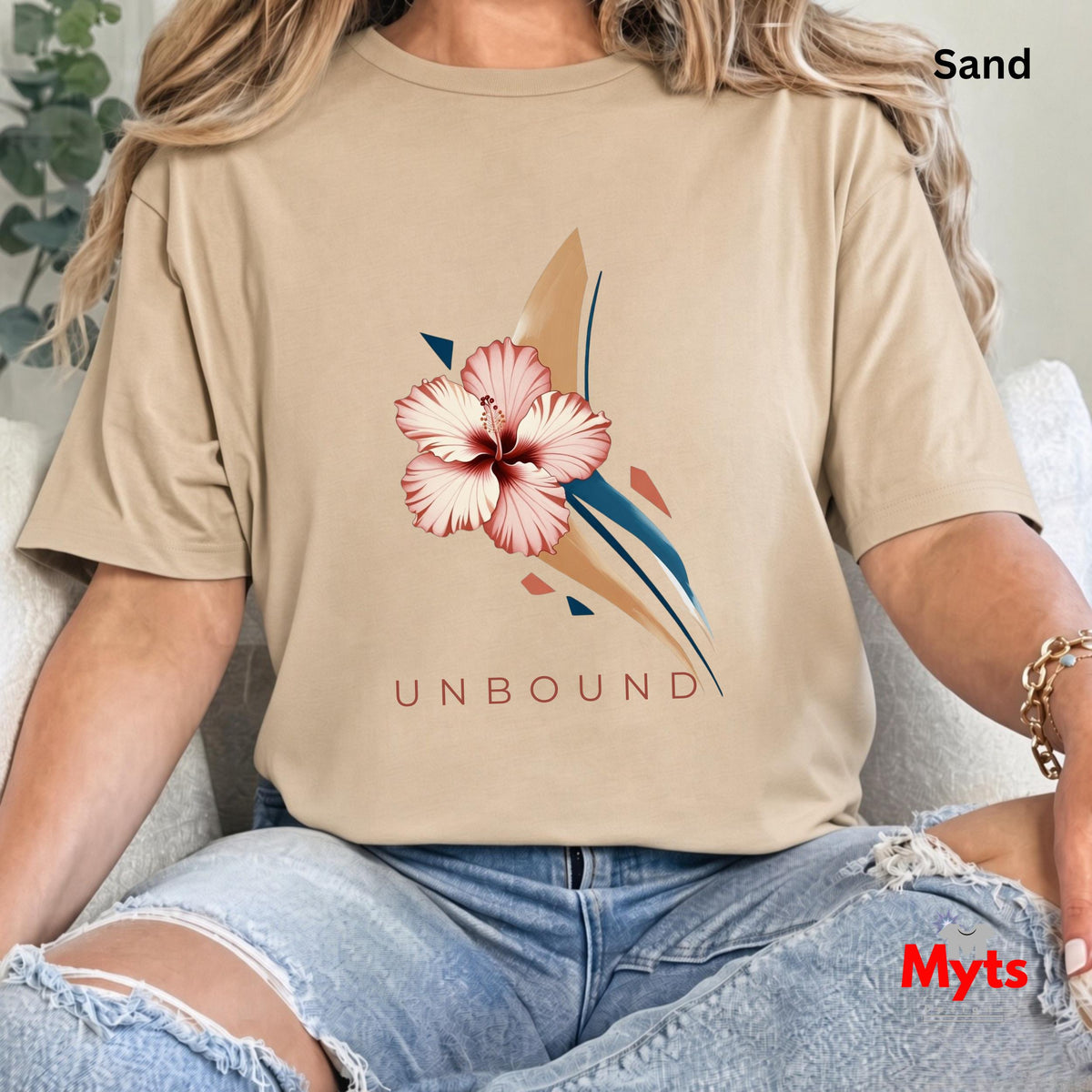 Close-up of a woman wearing a Sand UNBOUND hibiscus graphic T-shirt with distressed blue jeans.