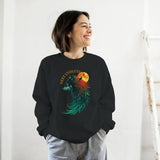A woman wearing a black crewneck sweatshirt with a colorful graphic of a wolf and a full moon, paired with gray sweatpants, standing against a white wall.