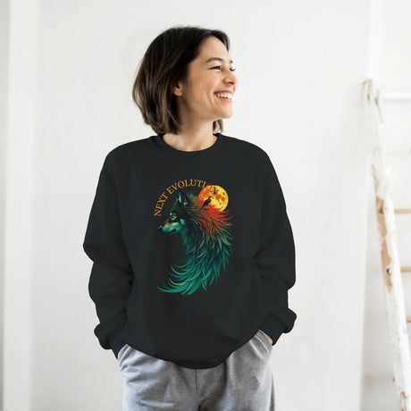 A woman wearing a black crewneck sweatshirt with a colorful graphic of a wolf and a full moon, paired with gray sweatpants, standing against a white wall.