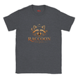 A dark heather gray crewneck t-shirt featuring a graphic of a raccoon's face with a moon and stars above it, and the text 'RACCOON' and 'STAY WILD' printed below in orange.