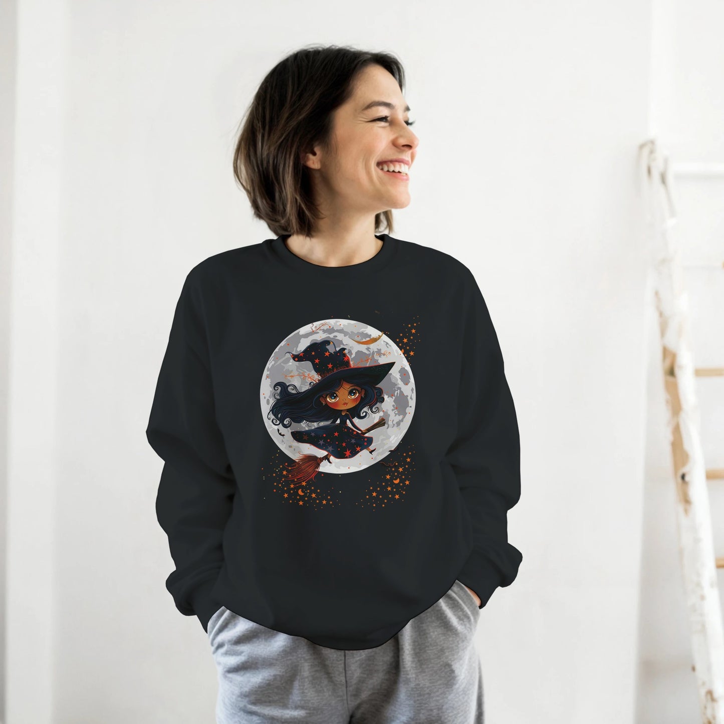 Person wearing a black sweatshirt with a Halloween-themed design of a witch and moon.