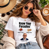 Woman reclining in white Know Your Parasites political humour graphic T-shirt with sunglasses, jeans and cream cardigan.