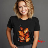 A woman wearing a black short-sleeve t-shirt with a graphic of autumn leaves in orange, red, and yellow, set against a solid gray background.