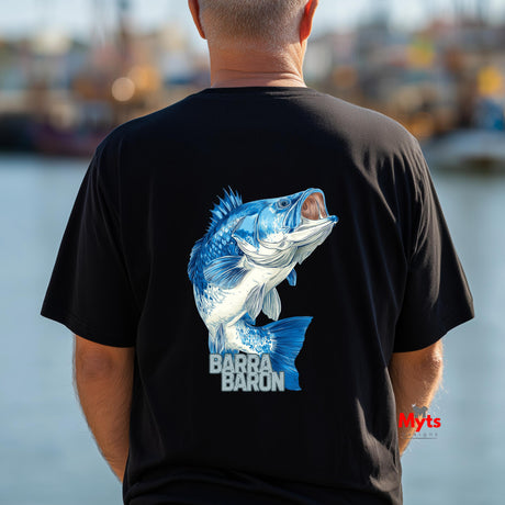 Person wearing a black t-shirt with a blue fish graphic and 'Barra Baron' text, standing by a body of water.