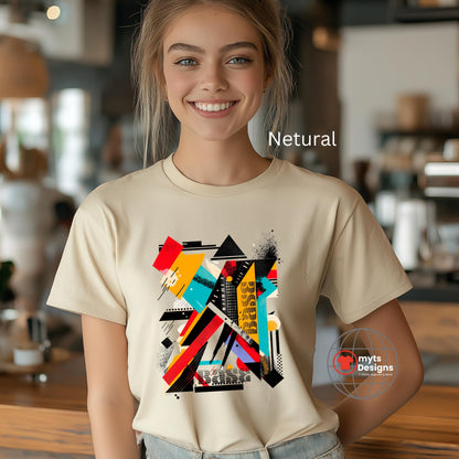 A natural beige t-shirt showcases a bold, abstract geometric design with overlapping colorful shapes in shades of red, teal, yellow, black, and white. The vivid and modern pattern creates a dynamic and artistic visual effect in the center of the shirt. The t-shirt is worn by a smiling woman standing indoors in a warmly lit, casual environment. A small red bird logo with the text “mytsDesigns” appears in the bottom right corner.