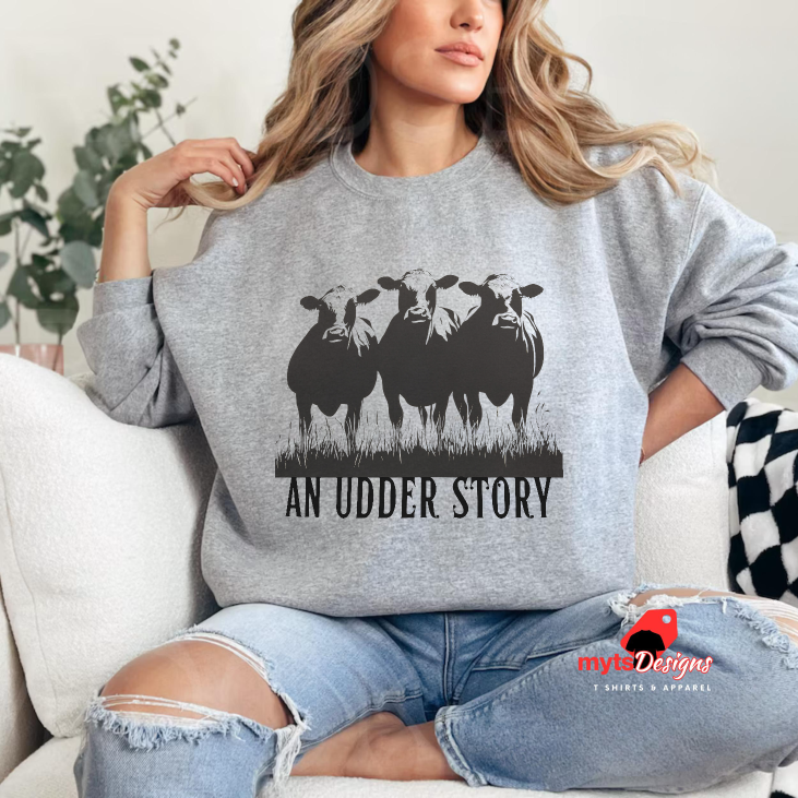 Person wearing a gray sweatshirt with cow graphic and 'An Udder Story' text, sitting on a couch.