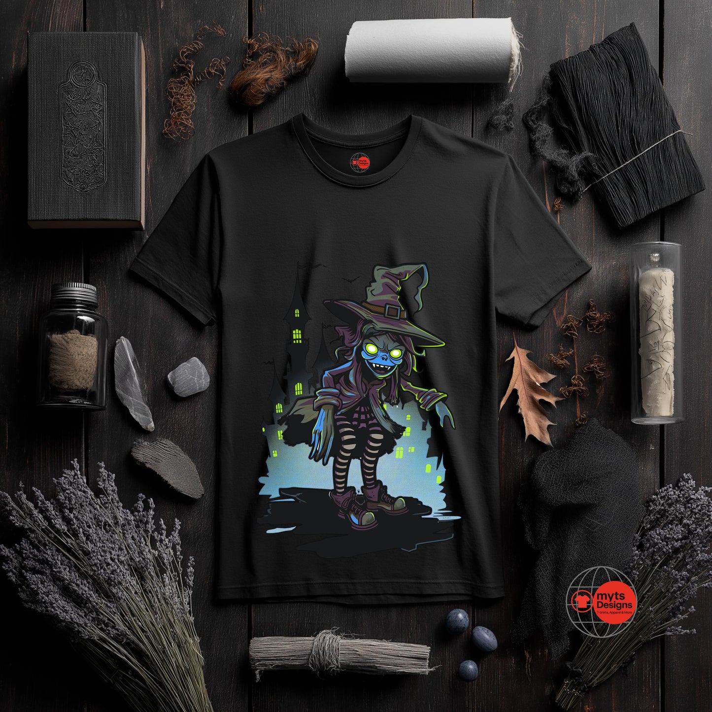 Black t-shirt with a colorful graphic of a witch on a dark wooden surface with Halloween-themed decorations.